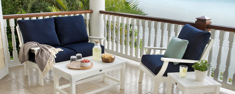 White Trex Outdoor Furniture Rockport accent tables and deep seating with navy blue cushions sit on a tile balcony overlooking water.