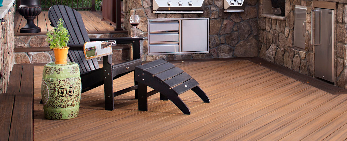 A black Trex Outdoor Furniture Yacht Club Shellback 2 Piece Adirondack Seating Set sits on a deck with stone cabinets.