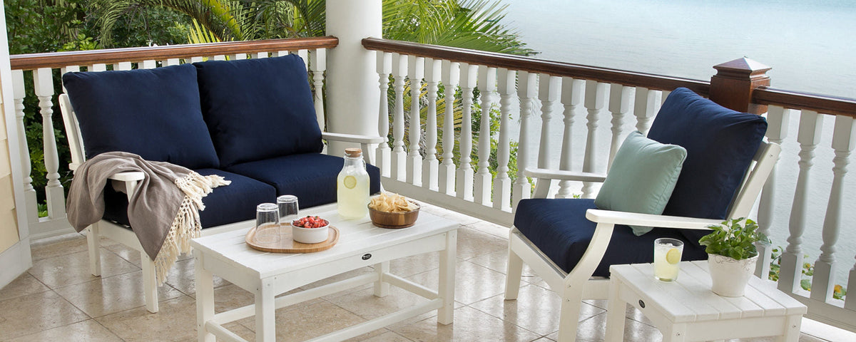 White Trex Outdoor Furniture Rockport accent tables and deep seating with navy blue cushions sit on a tile balcony overlooking water.