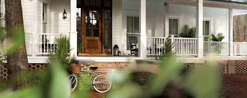 A white house with a wraparound porch and brick steps holds black Trex Outdoor Furniture Yacht Club Rockers.